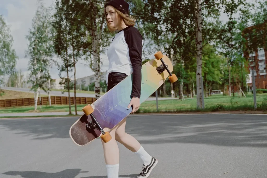A teenage girl carrying a longboard in a city park