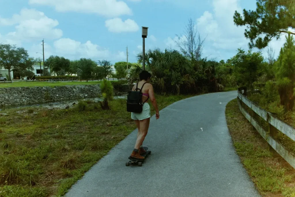 A woman riding a skateboard along a leafy paved path