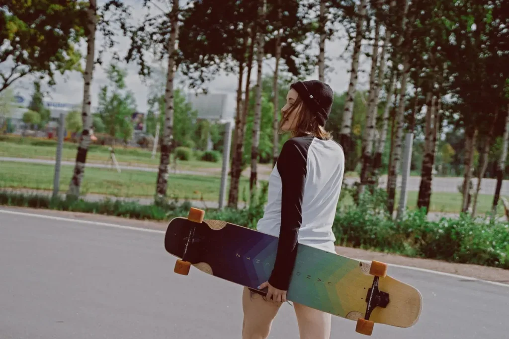 A young woman walking through a park with a longboard