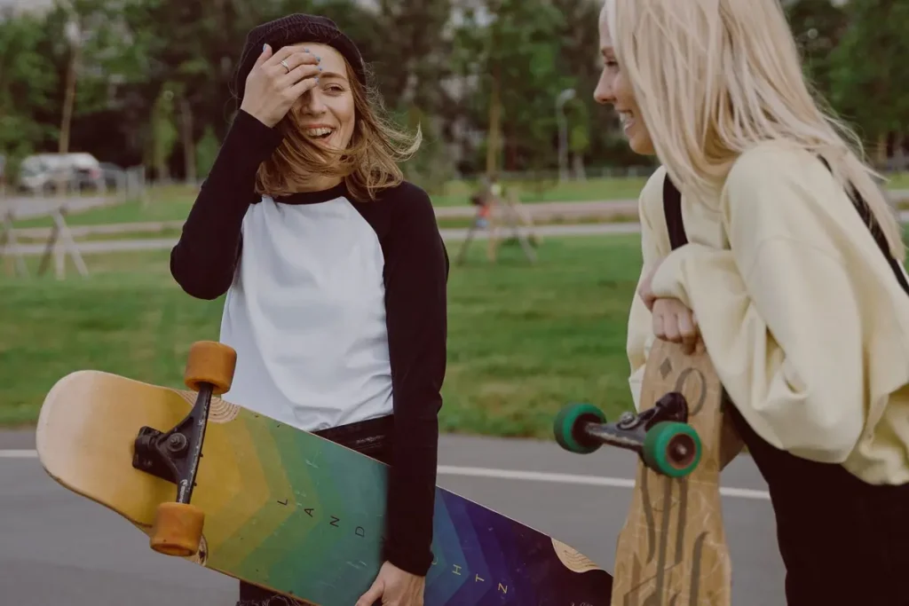 Two teenage girls laughing and holding longboards in a park