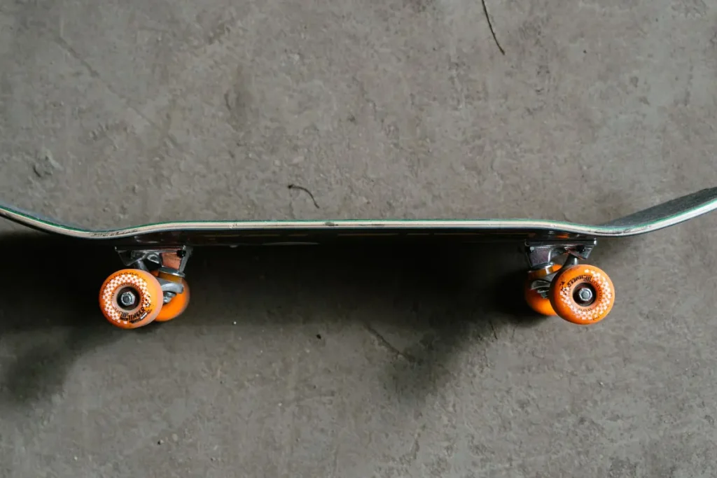 Close-up of a skateboard with orange wheels on a concrete floor
