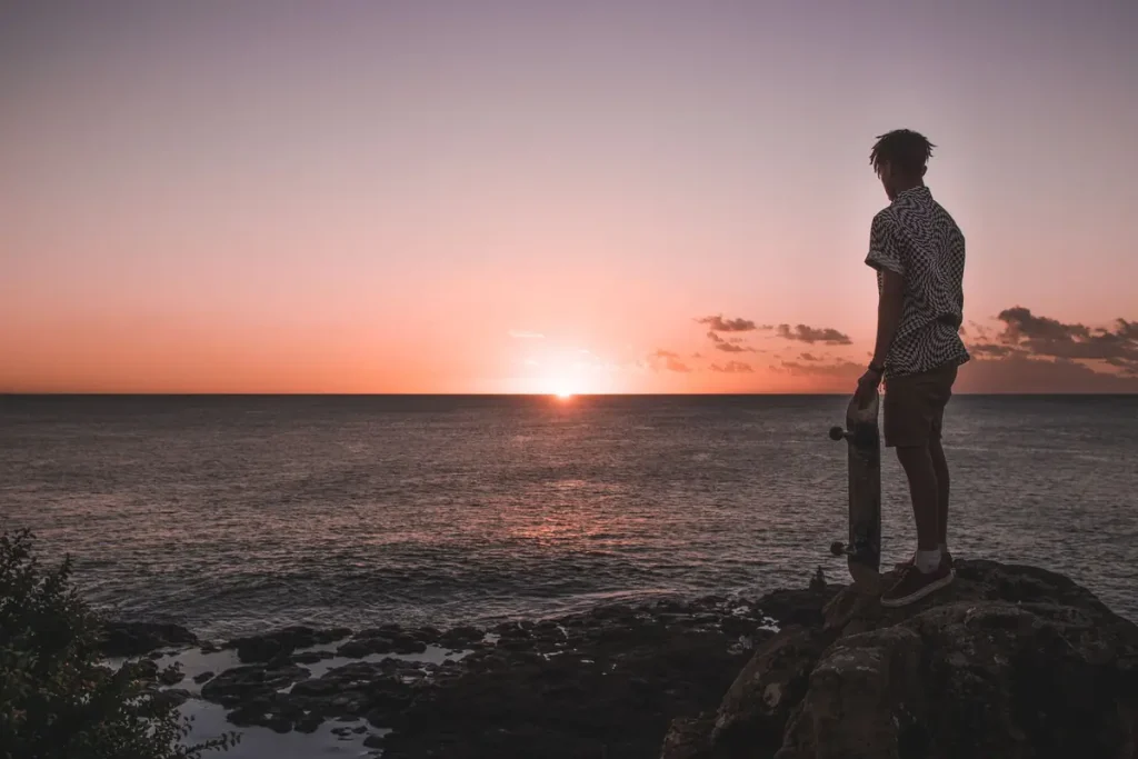 Silhouette of a man with a skateboard watching an ocean sunset