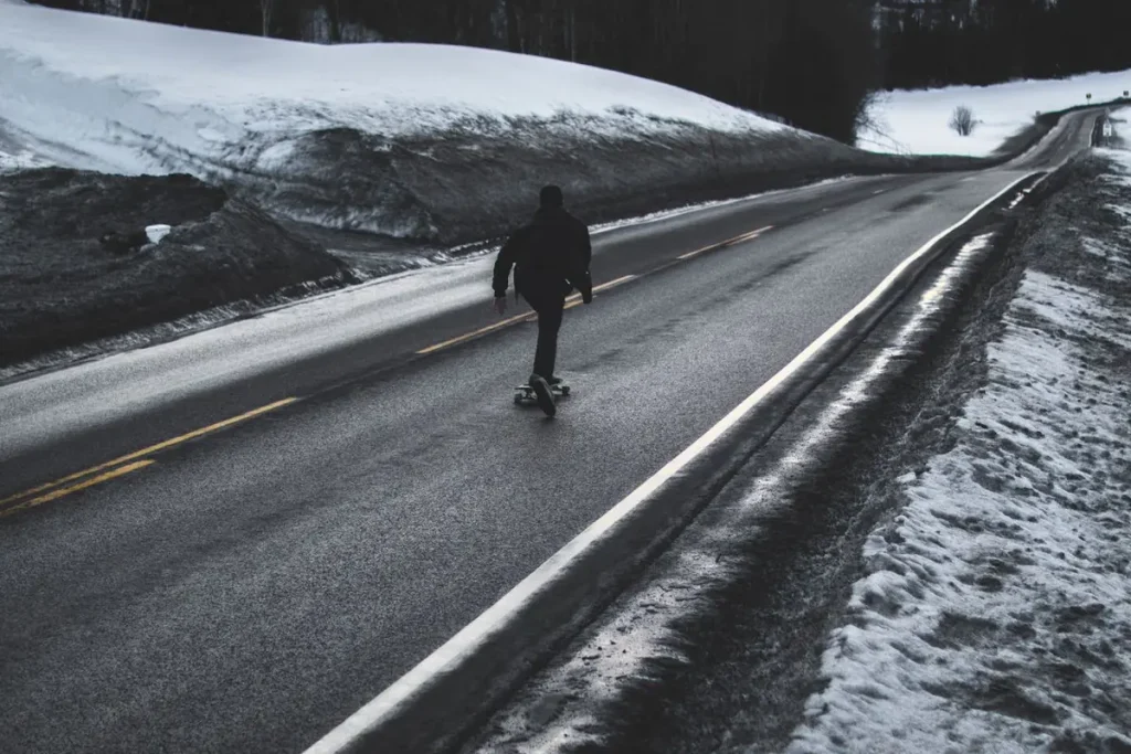 A skateboarder riding down a road with snow on both sides