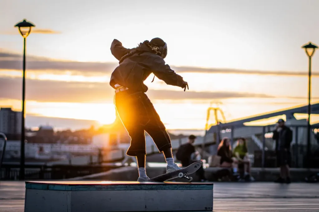 A skateboarder riding through an urban park at sunset
