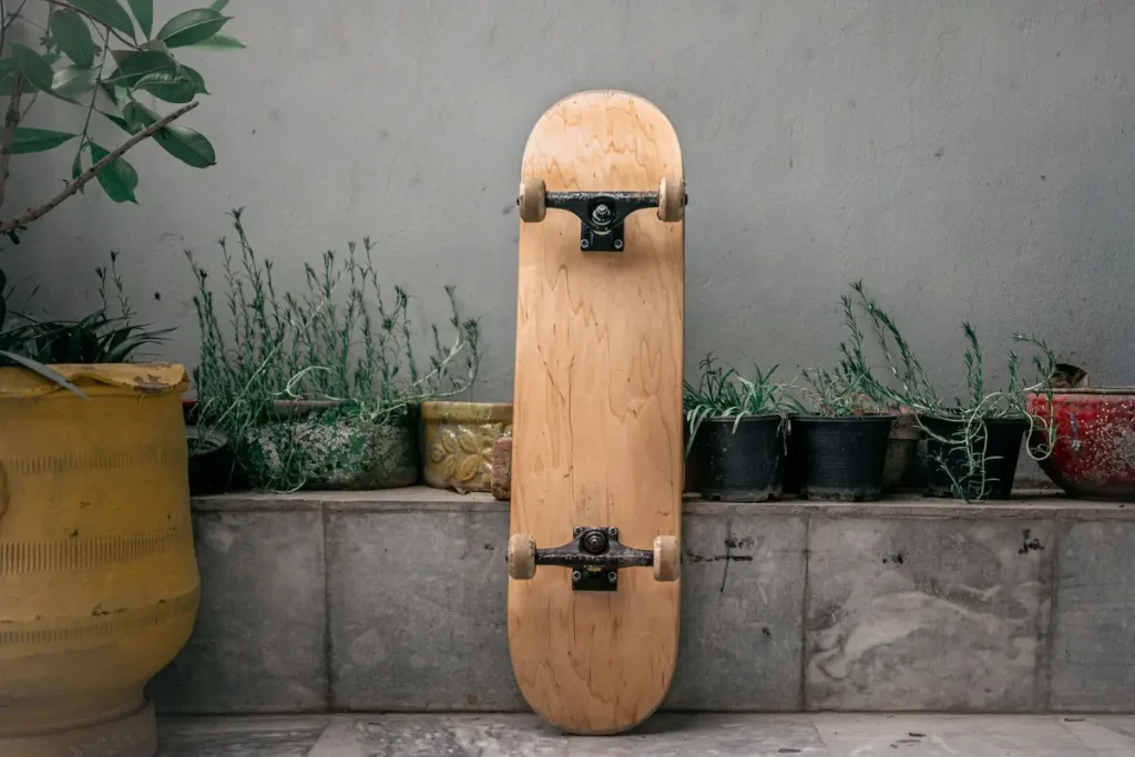 A wooden skateboard leaning against an outdoor planter