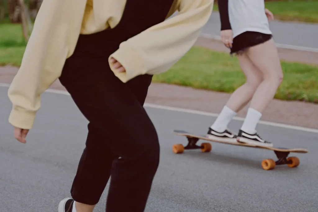 Two women riding longboards along a park path