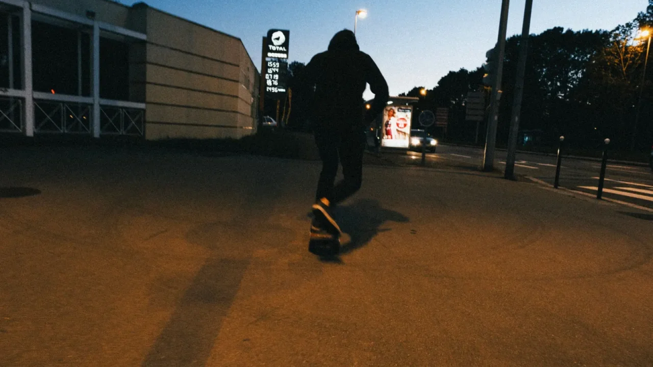 A skateboarder riding along a city sidewalk at dusk