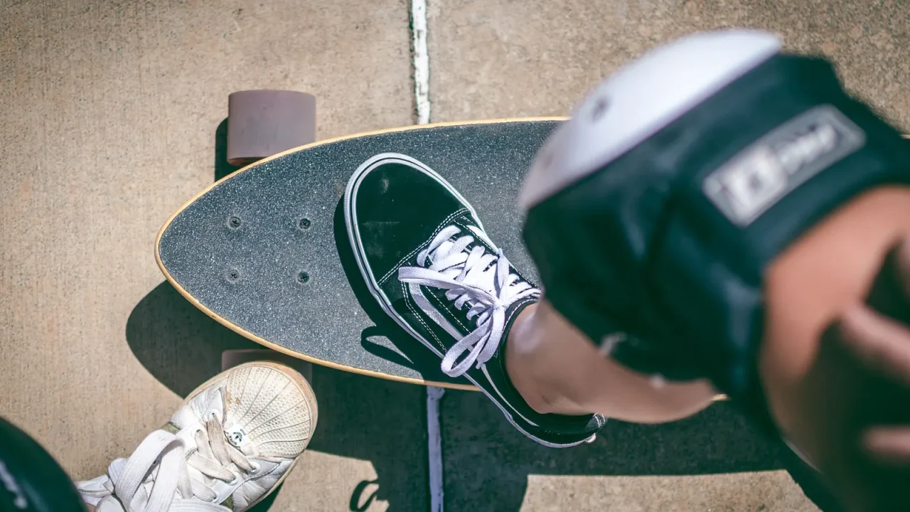 Close-up from above of a rider's shoes on a longboard and a knee pad