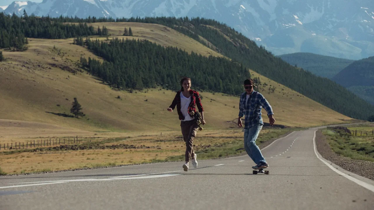 Two people skateboarding and running down a mountain road