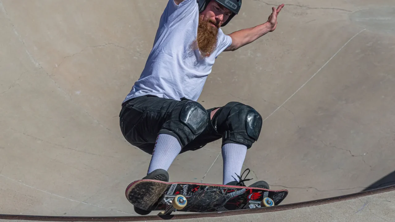 An adult skater balancing on a longboard in a round skatepark
