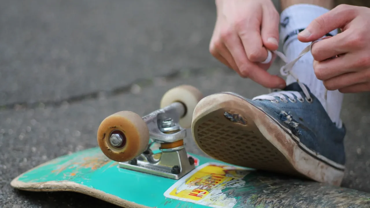 A skateboarder tying a shoelace while sitting on a street