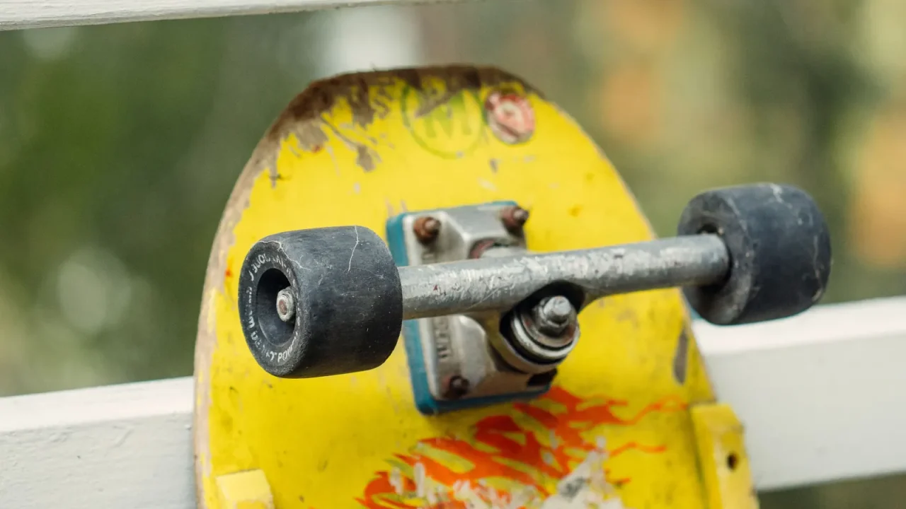 An old skateboard with a yellow deck, showing its trucks and wheels